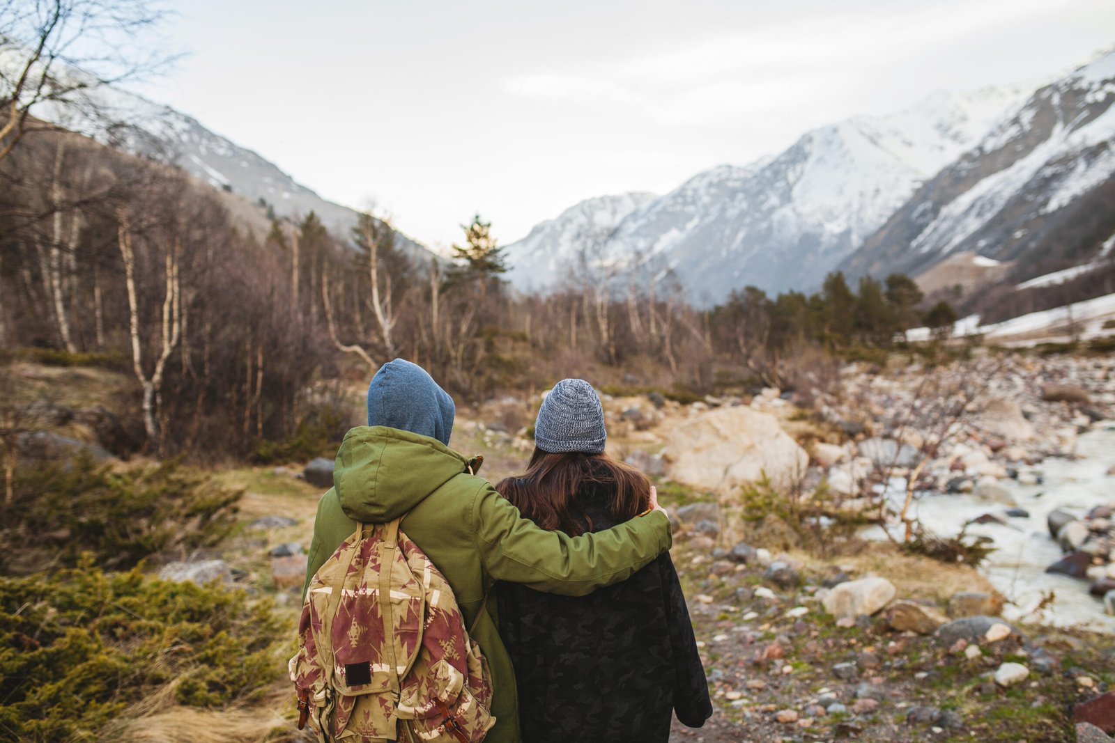 young beautiful hipster man and woman in love traveling together in wild nature, hiking in forest, autumn style apparel, coat, romance, vacation, embracing, view from back, backpacker